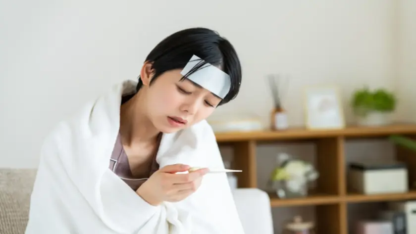 体温計で発熱を確認してつらそうな女性