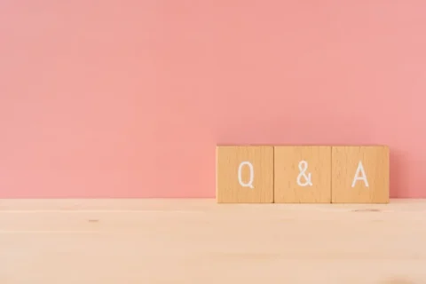 木でできたQ&Aの文字　が明るいピンクの背景の前に並んでいる