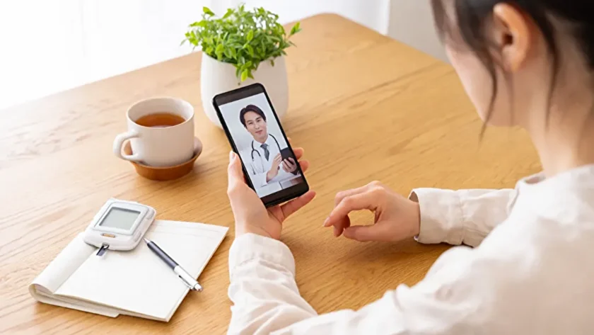 スマホでオンライン診療を受ける患者　紅茶や観葉植物、測定器、ノートが並ぶ明るい窓際のテーブル