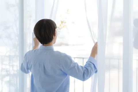 朝カーテンを開けて朝日を浴びる女性