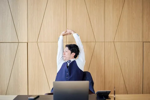 パソコンの前で大きく伸びをする男性 デジタルデトックス