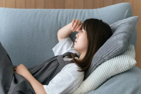 ソファに横になって片頭痛の症状が治まるのを待っている女性