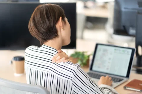 体のだるさが仕事中も抜けない女性の後ろ姿